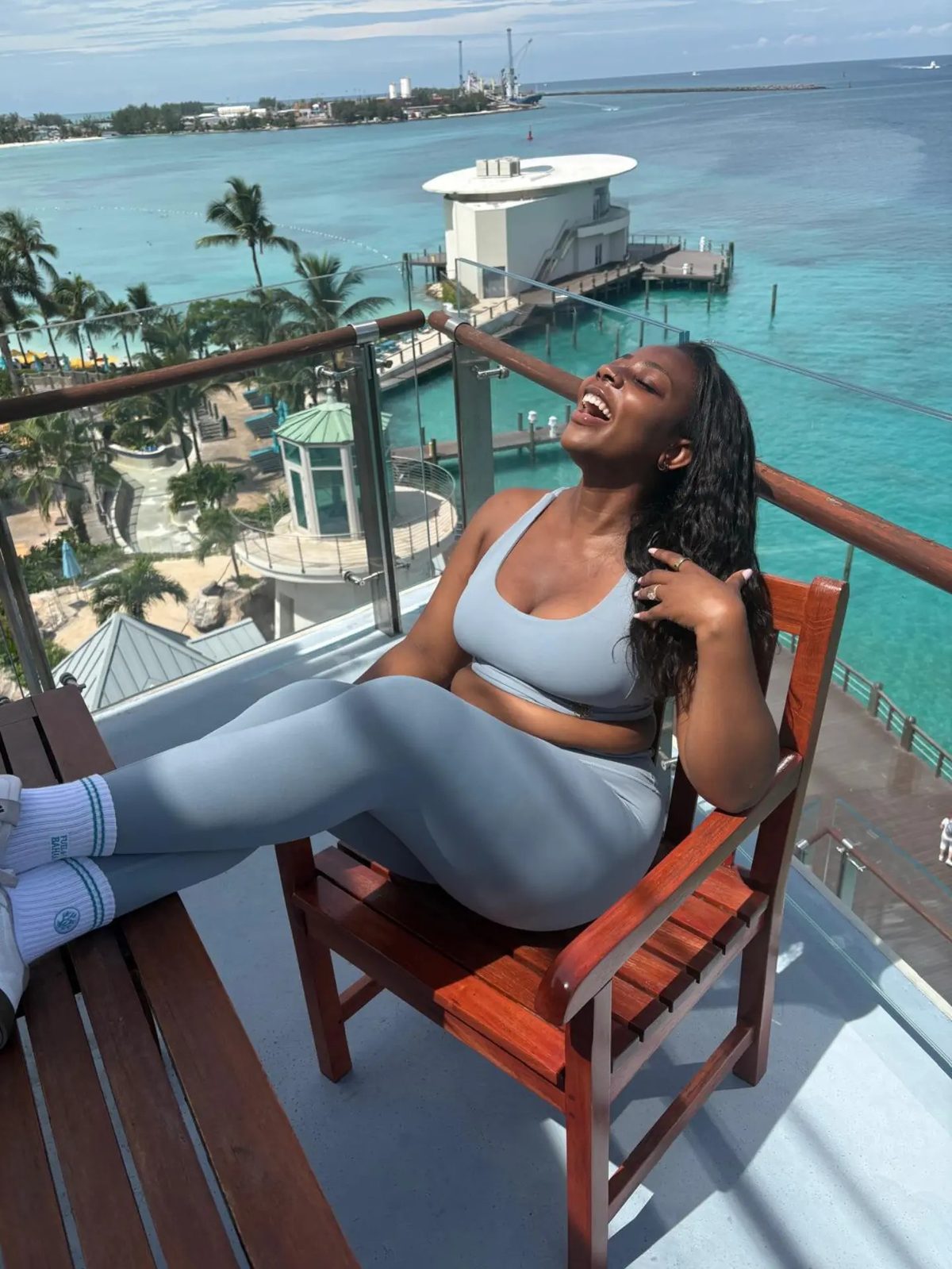 A woman in grip socks laughing on a balcony chair above turquoise water