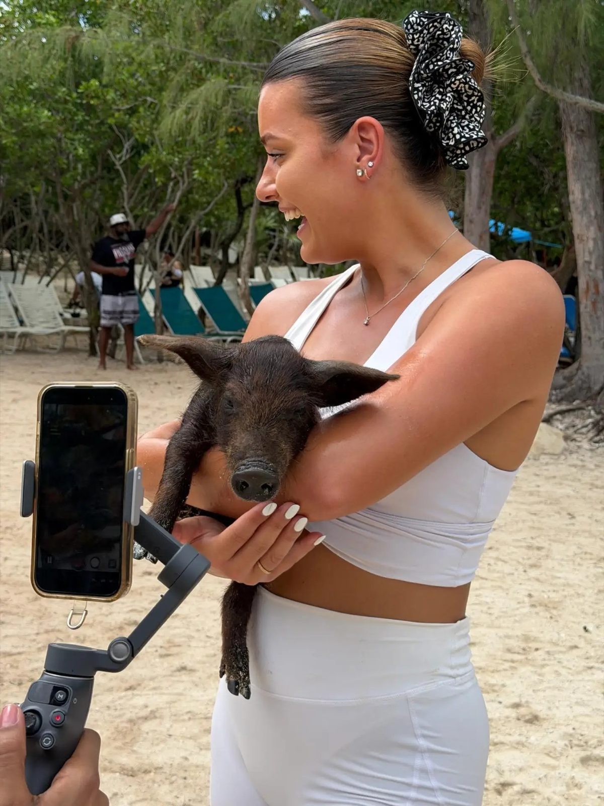A woman in white activewear holding a small pig on a Bahamian beach