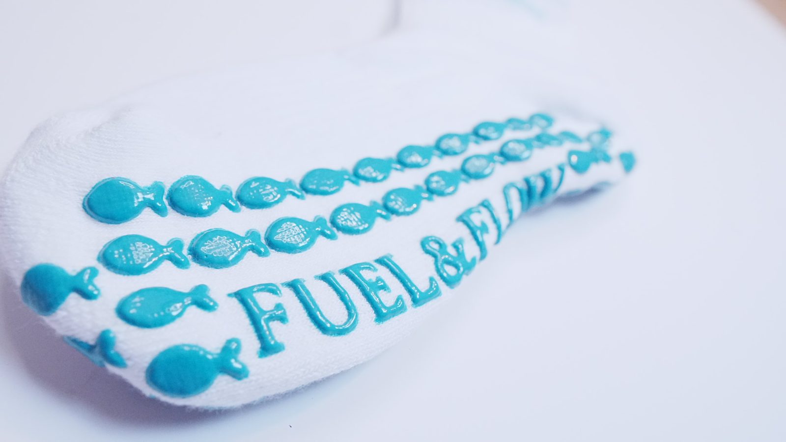 Close-up of the teal fish-shaped grips and the Fuel & Flow lettering on a white grip sock