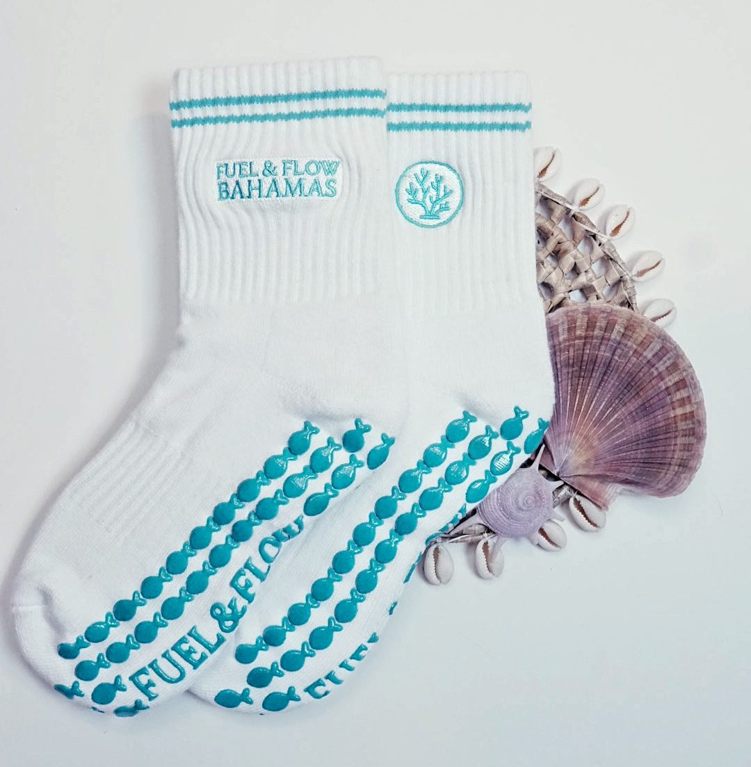 Fuel & Flow grip socks with a coral mark and teal fish-shaped grips, laid out beside sea shells