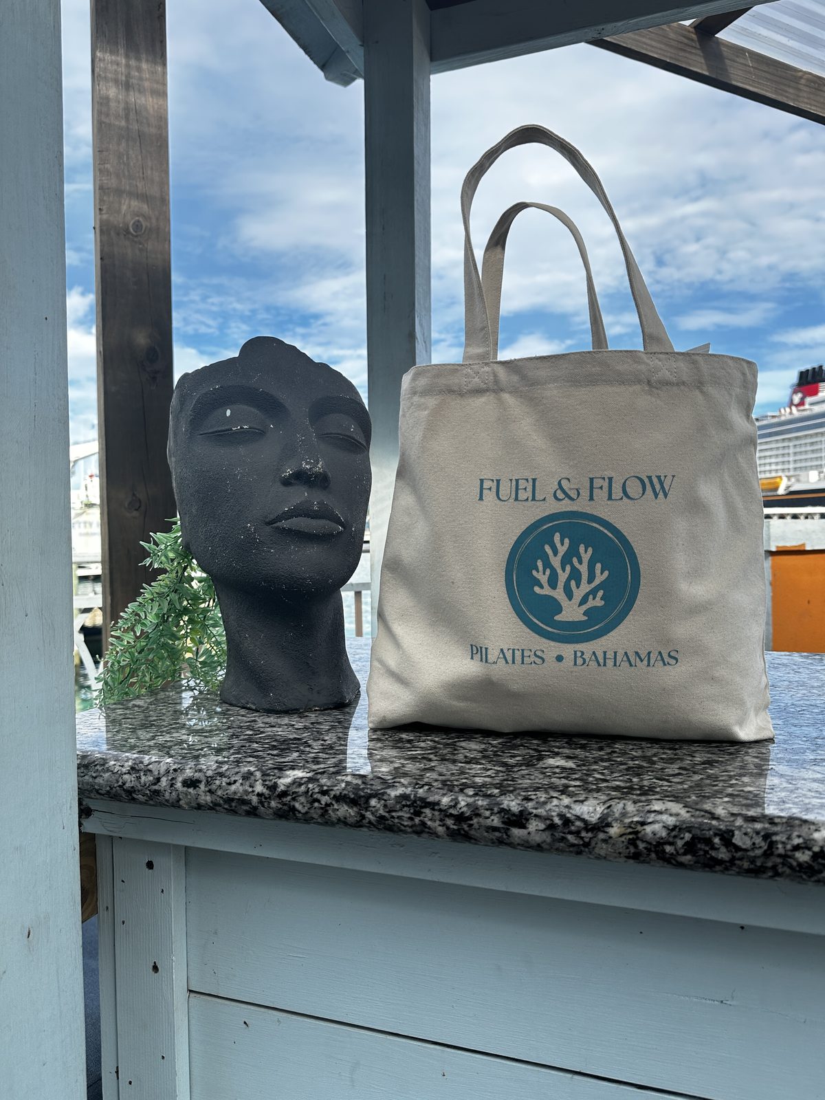 A natural canvas Fuel & Flow Pilates Bahamas tote on a counter by the water
