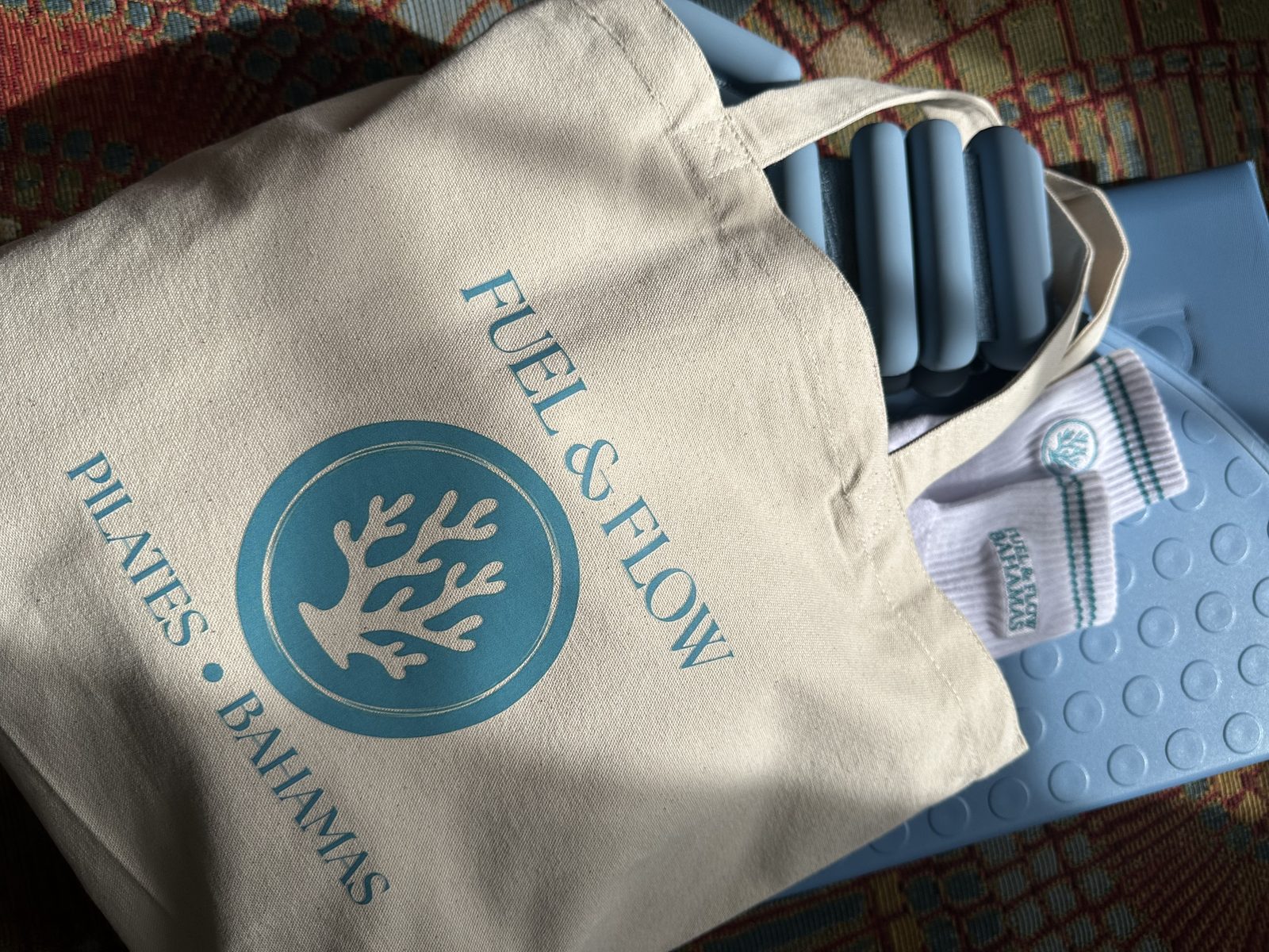 A natural canvas Fuel & Flow Pilates Bahamas tote with grip socks tucked in the top